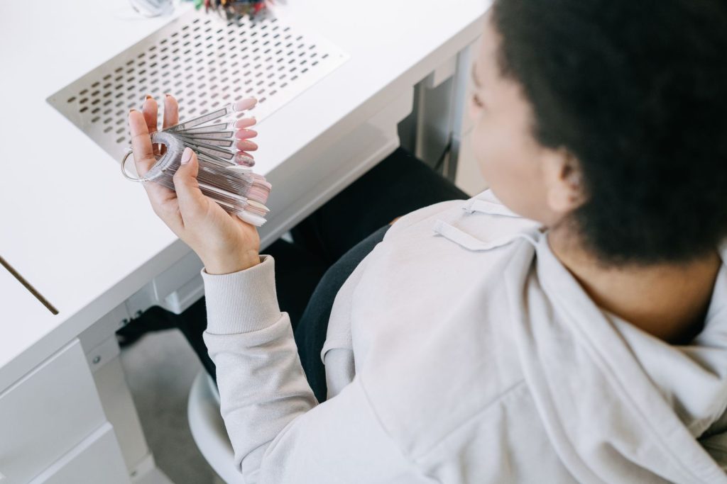 Pregnant woman holding nail polish samples, exploring manicure options.