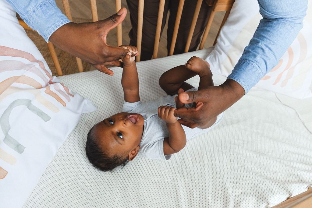 A tender moment showing a father lovingly holding his baby's hand while the baby lies in a crib.