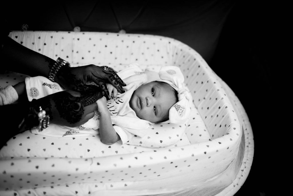 Black and white photo of a newborn in a crib with adult's hands, artistic tone.