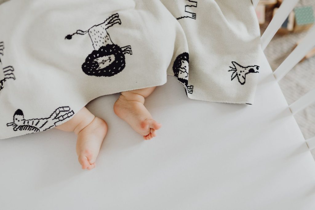 A close-up of a baby's feet poking out from under a blanket with animal prints, lying in a crib.