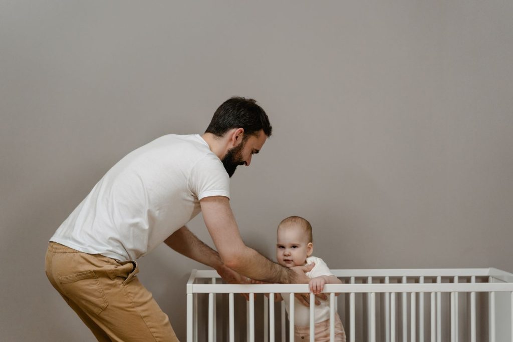 A father attentively interacts with his baby in a crib, showcasing modern parenting at home.
