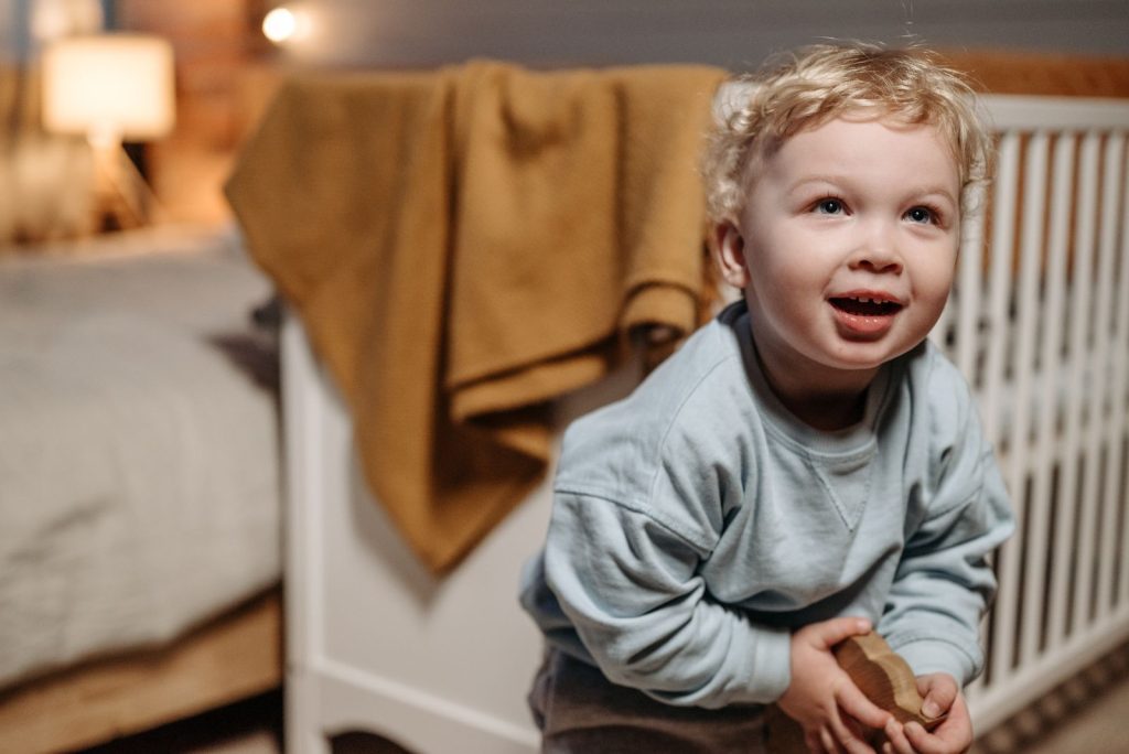 Cute child with blond hair in a cozy room playing with a wooden toy and smiling.