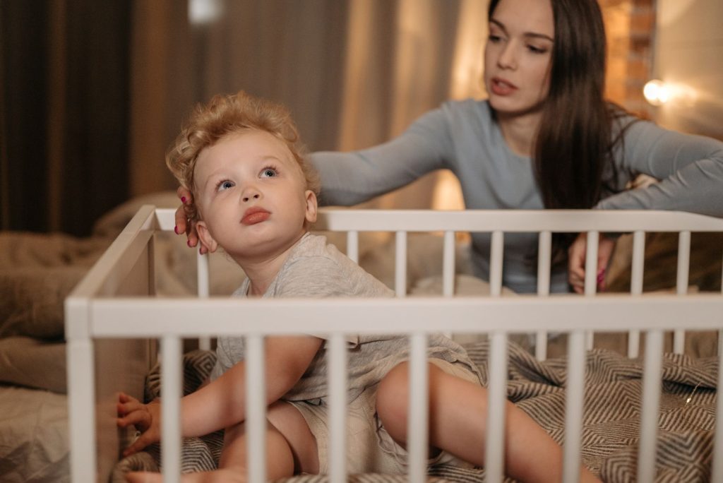 A mother watching over her toddler in a crib during a cozy evening at home.