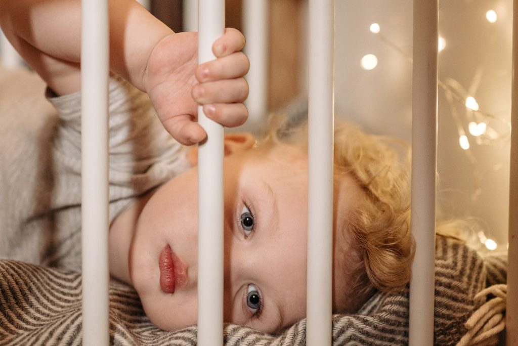 Cute baby lying in a crib with soft lighting and warm ambiance indoors.