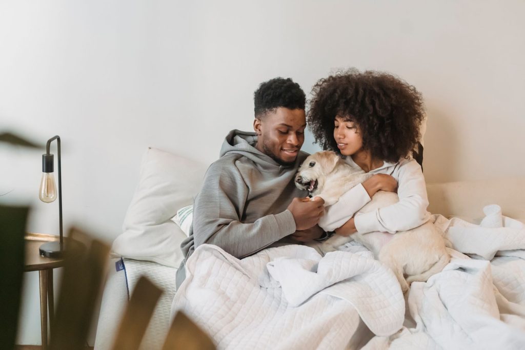 Happy African American couple with cute white dog resting on cozy bed at home