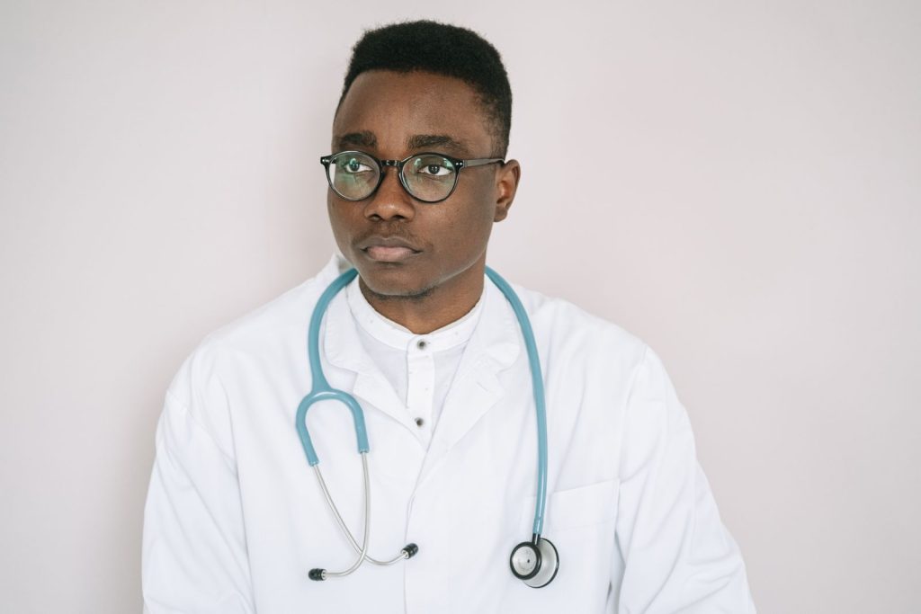 Portrait of a serious doctor with eyeglasses, stethoscope, and white coat indoors.
