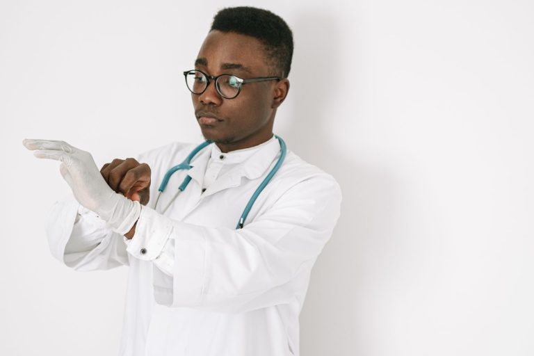 A focused doctor in a medical gown and eyeglasses putting on gloves, symbolizing professionalism.