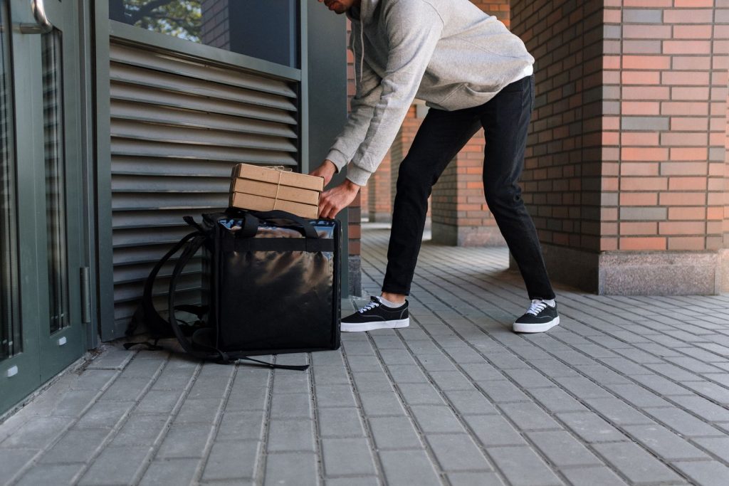 Courier placing packages in delivery bag outside a residential building.