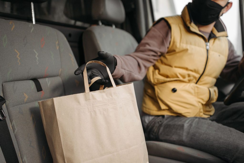 Masked courier provides safe contactless delivery from inside vehicle.