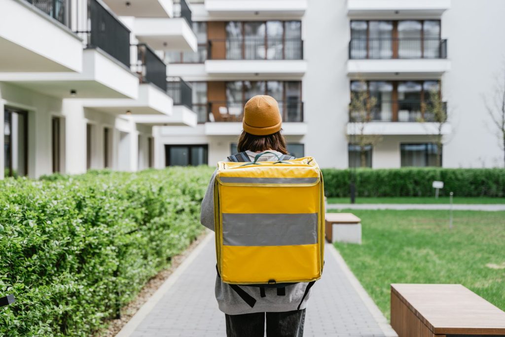 Rear view of a courier carrying a yellow delivery bag in an urban area.