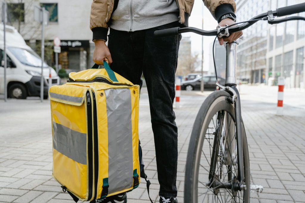 Food delivery cyclist in city holding a large thermal bag, ready for service.