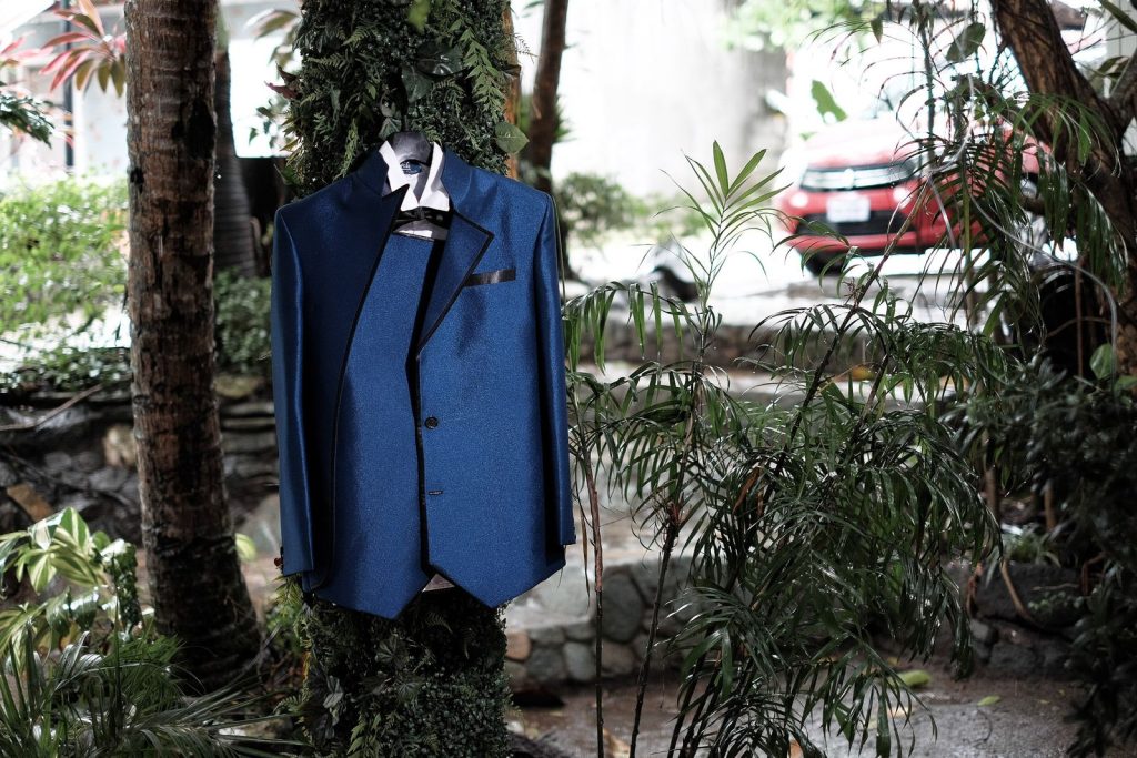 A stylish blue suit elegantly hangs on a tree outdoors, surrounded by lush greenery.