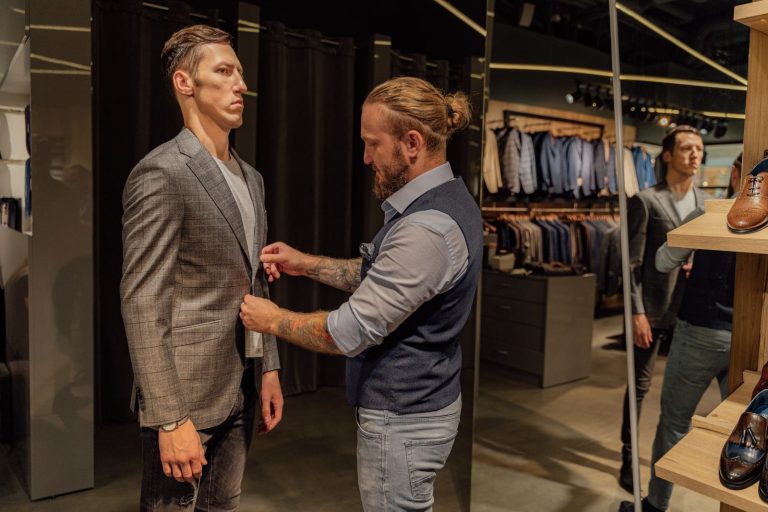 A tailor adjusts a man's suit jacket in a modern fashion store.