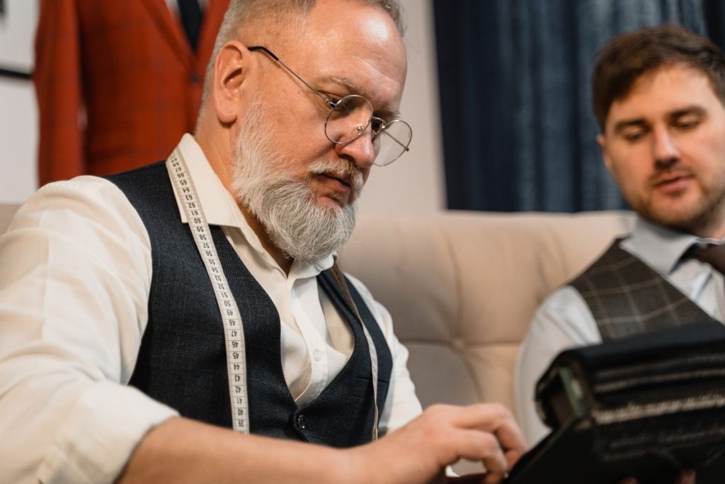 Experienced tailor working in clothing atelier, measuring a suit with tape measure.