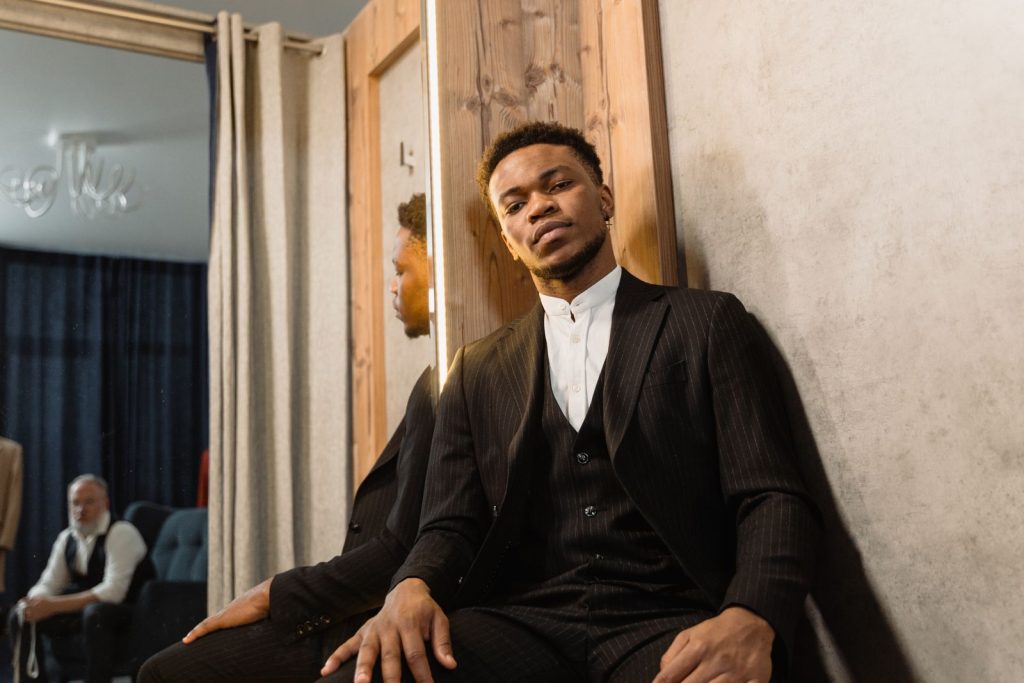 Confident man in a black suit sitting in a stylish indoor setting, reflecting elegance and poise.