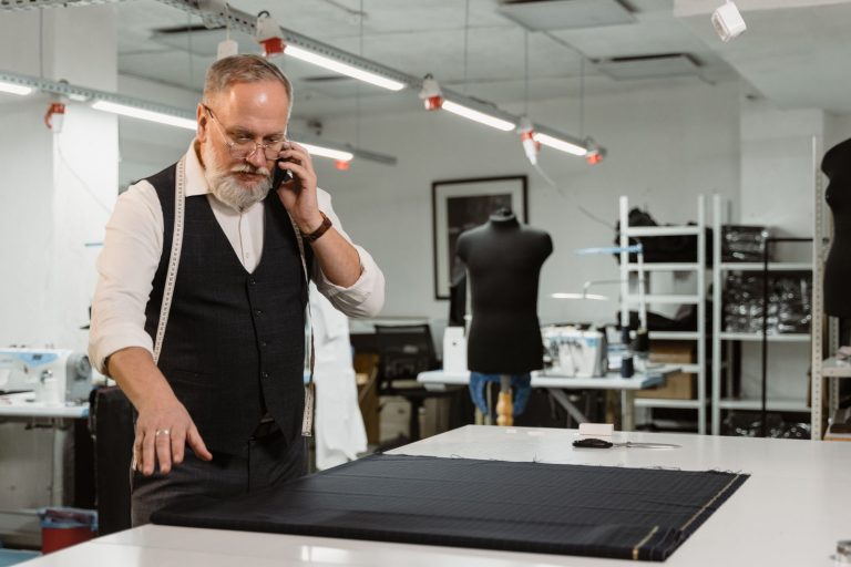 Experienced tailor examining fabric in a fashion atelier while on the phone.