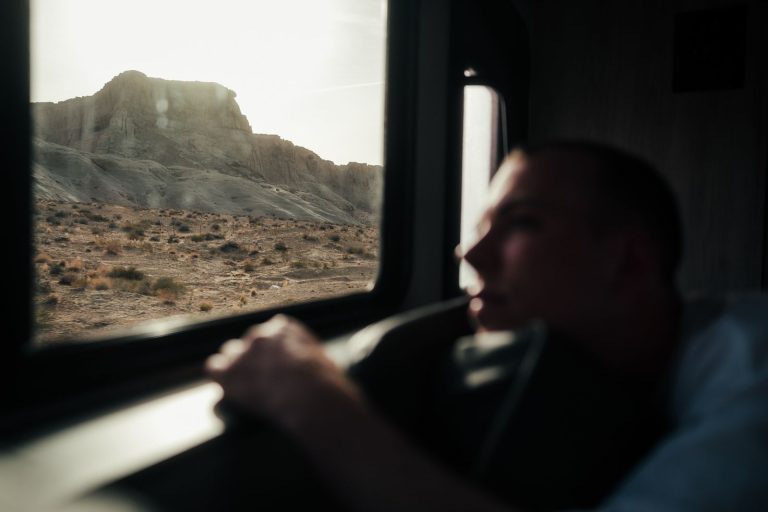 A person gazes out a vehicle window at a rugged mountain landscape, capturing solitude and wanderlust.