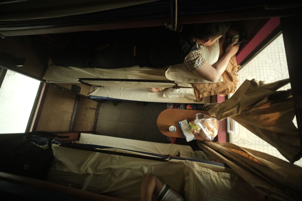 Top view of individuals resting on train bunks with travel essentials.