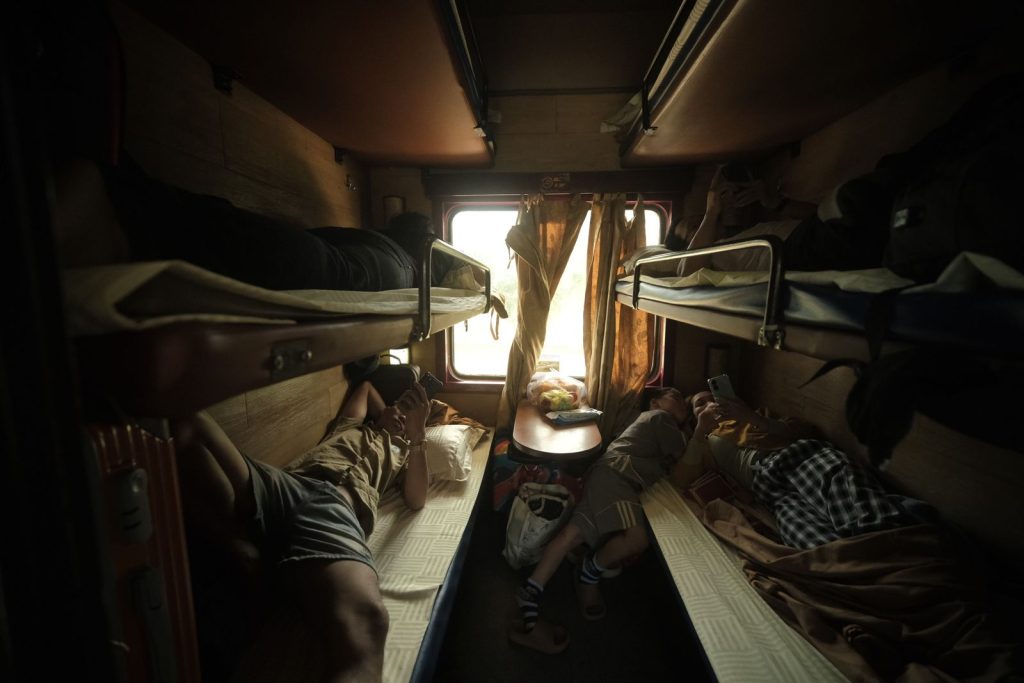 Passengers resting in a cozy train cabin with bunk beds and a window view.