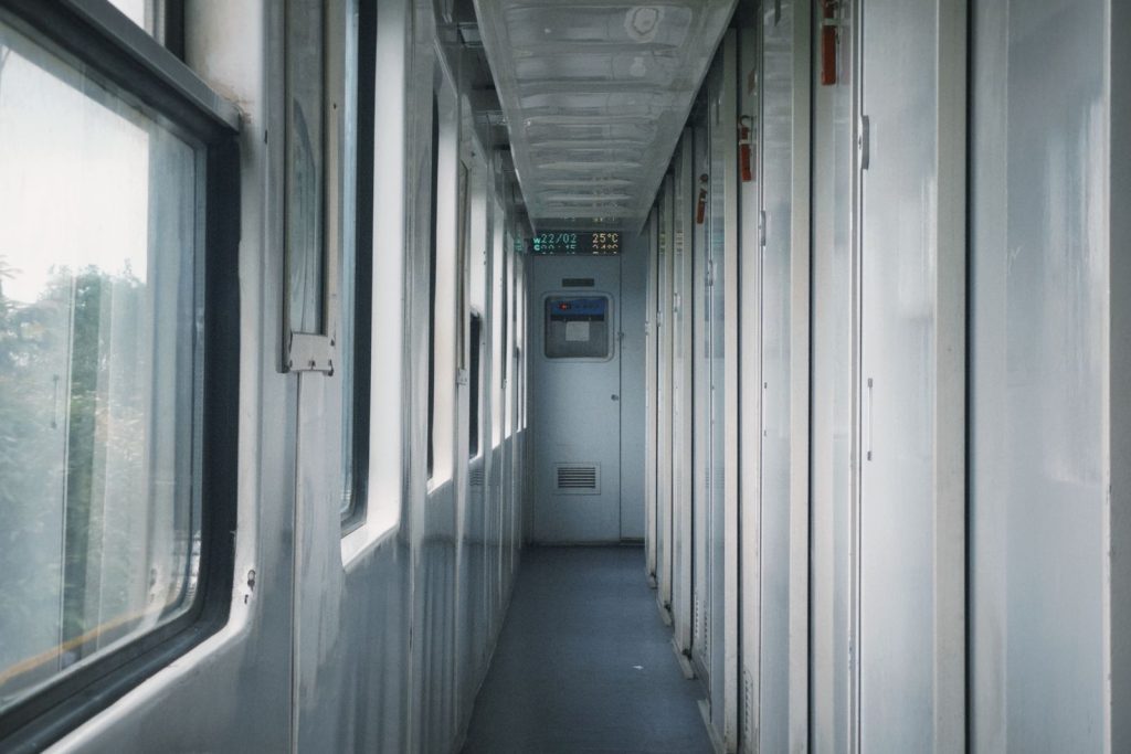 A narrow, well-lit corridor inside a train, featuring doors and windows.