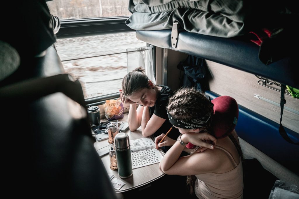 Two women enjoy solving puzzles during a relaxing train ride, capturing a moment of thoughtful leisure.