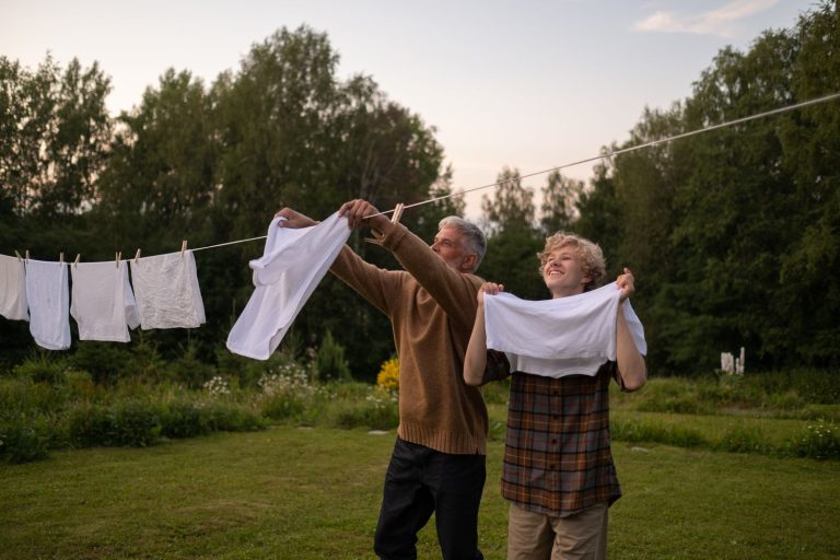 A joyful moment as grandfather and grandson hang laundry on a line in a lush summer garden.