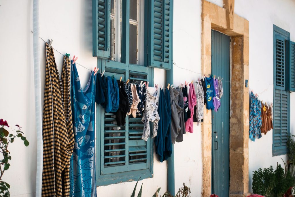 Vibrant clothes hang on a line against rustic shutters and a stone wall.