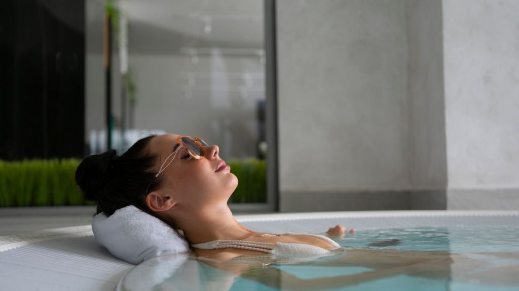 Woman in a swimsuit enjoying relaxation in an indoor jacuzzi with closed eyes.