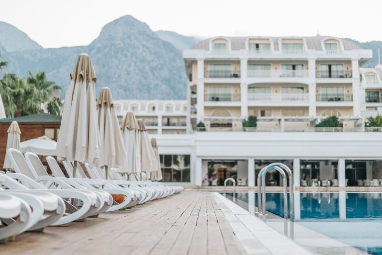 Empty sunloungers and umbrellas by a luxury resort pool with a mountain view.