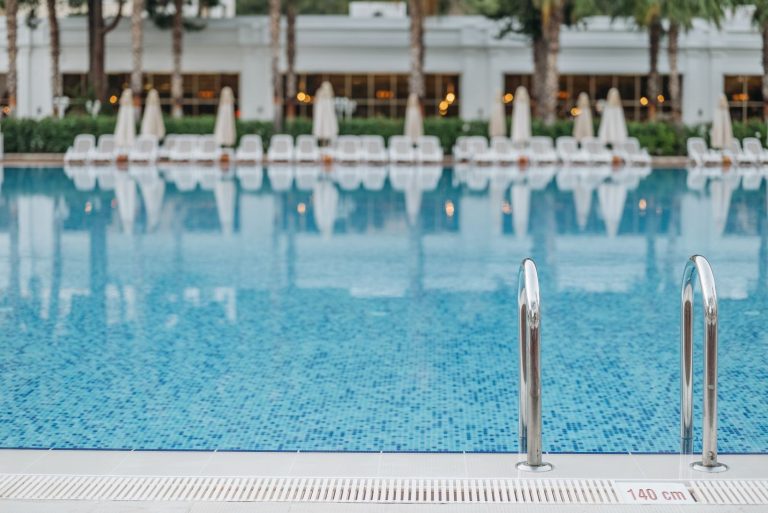 Bright and tranquil view of a resort swimming pool with ladder and deck chairs.