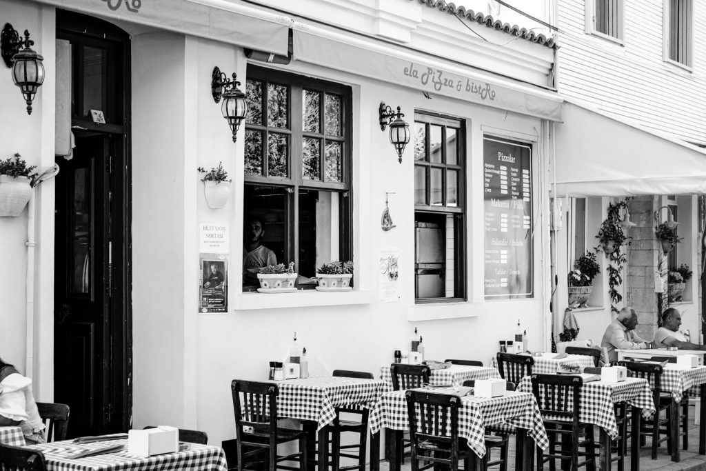 A black and white photo of a cozy outdoor restaurant in Bozcaada, Turkey, showcasing tables and diners.