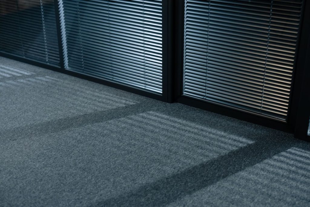 A serene indoor space with shadows and venetian blinds casting lines on a carpeted floor.