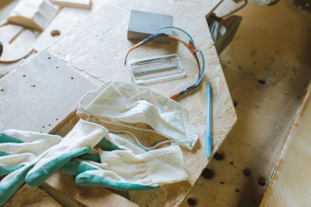 Close-up of safety equipment including gloves, mask, and goggles on a woodworking table.