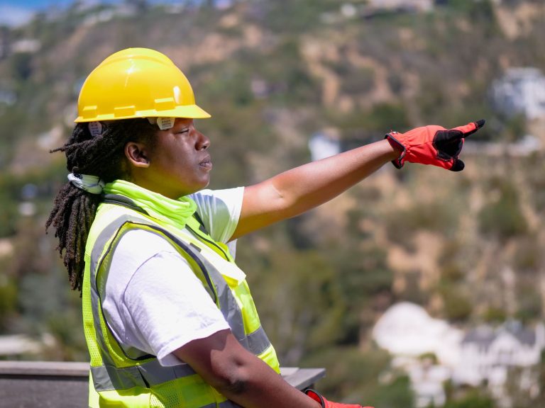 Black female engineer outdoors pointing ahead, wearing safety gear.
