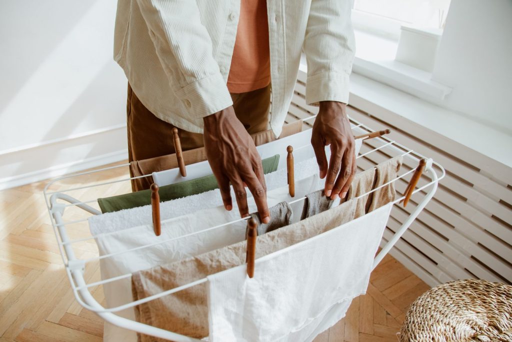 A man hangs freshly washed laundry on a drying rack in a sunny room.