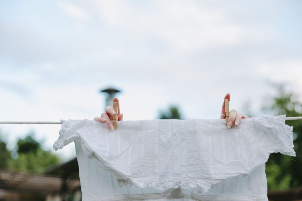 Close-up of hands pinning a white blouse on a clothesline outside on a sunny day.