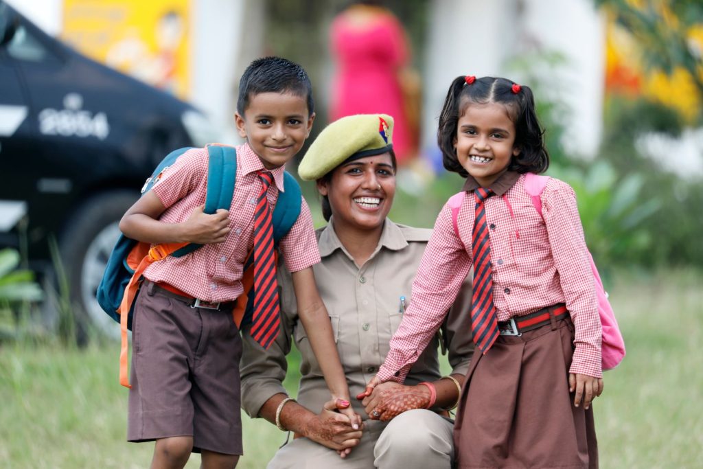 A cheerful schoolboy and schoolgirl enjoy a day with a smiling police officer outdoors.