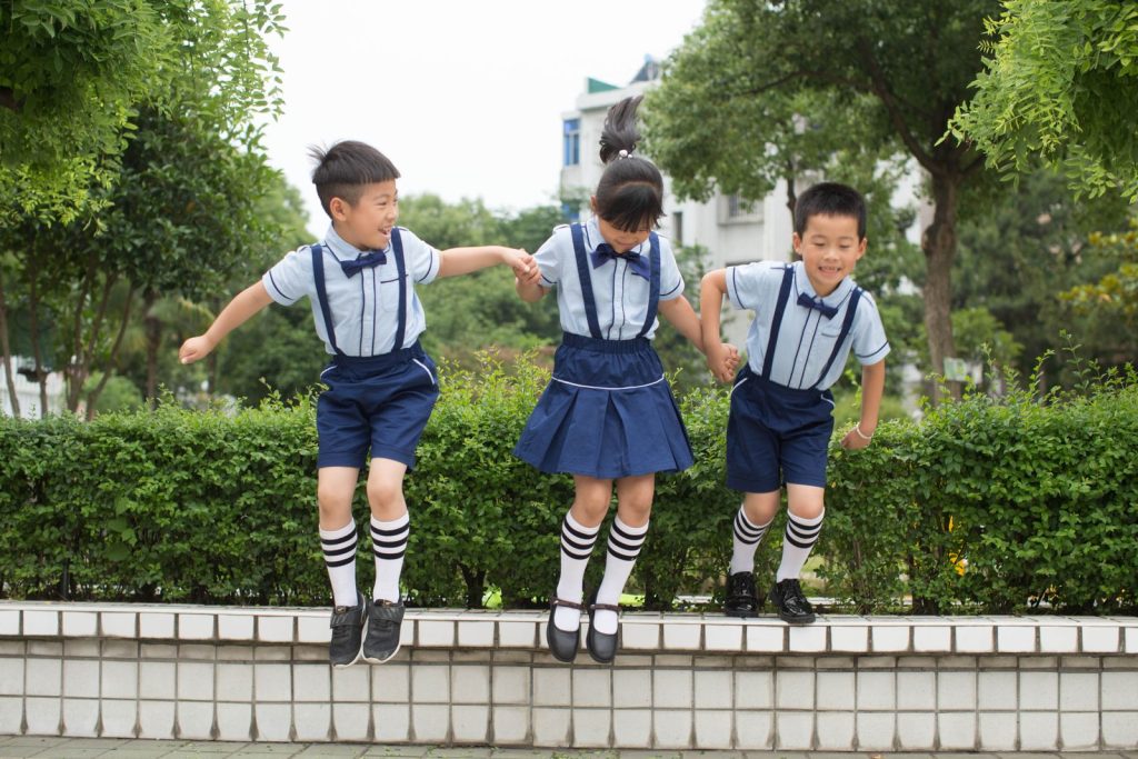 Three cheerful children in matching uniforms jump outdoors, enjoying a playful moment.