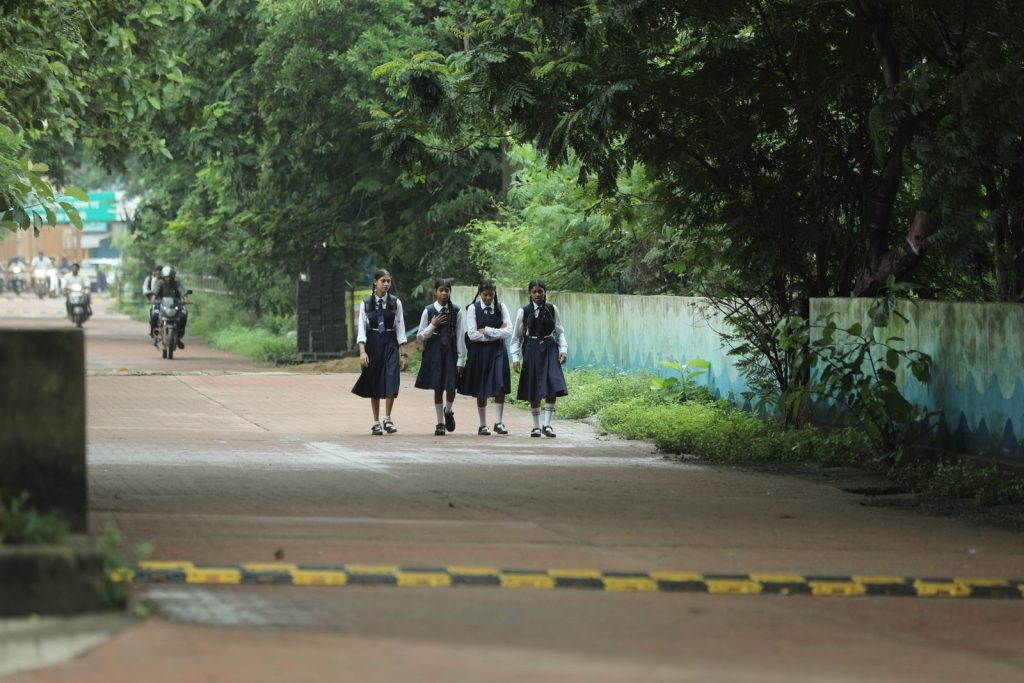 Four schoolgirls in uniform walking on a tree-lined path in Raipur, India.