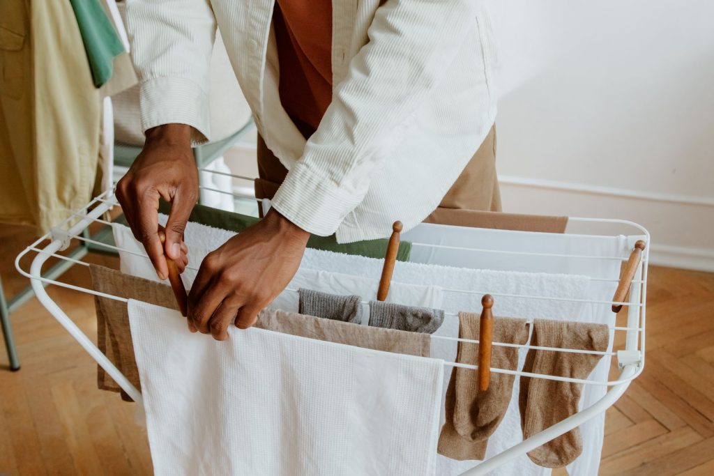 A person hanging clean laundry on an indoor drying rack.