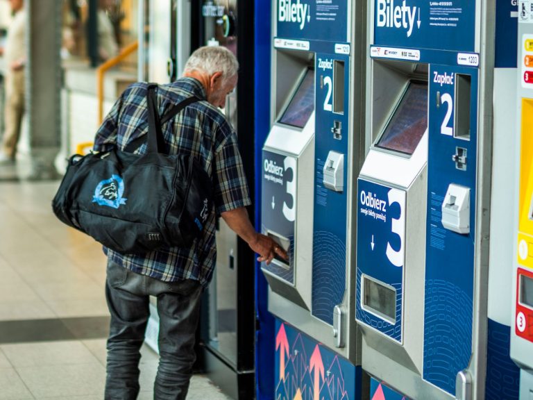 Senior male purchasing ticket from vending machine in public indoor area.