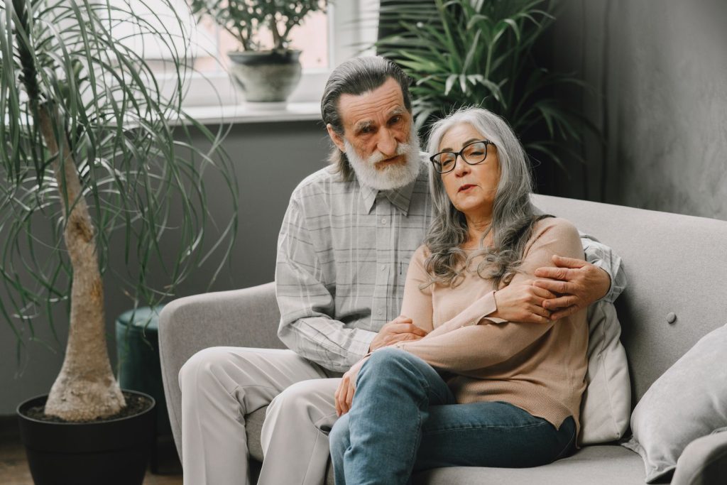 An elderly couple warmly embraces on a cozy sofa, surrounded by lush indoor plants, creating a serene ambiance.