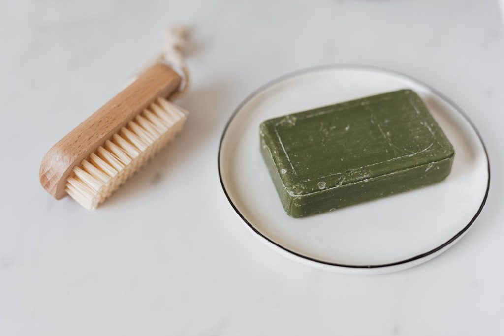 Minimalist photo of a green organic soap and wooden brush on marble for natural care.