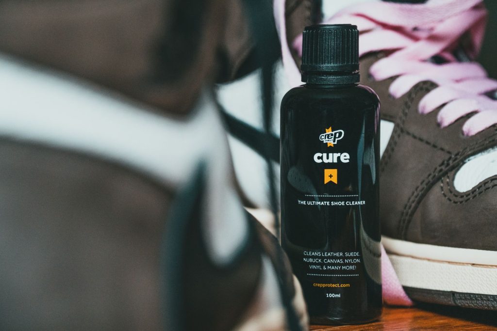 Closeup of trendy brown suede sneakers and bottle of shoes care product in black plastic bottle