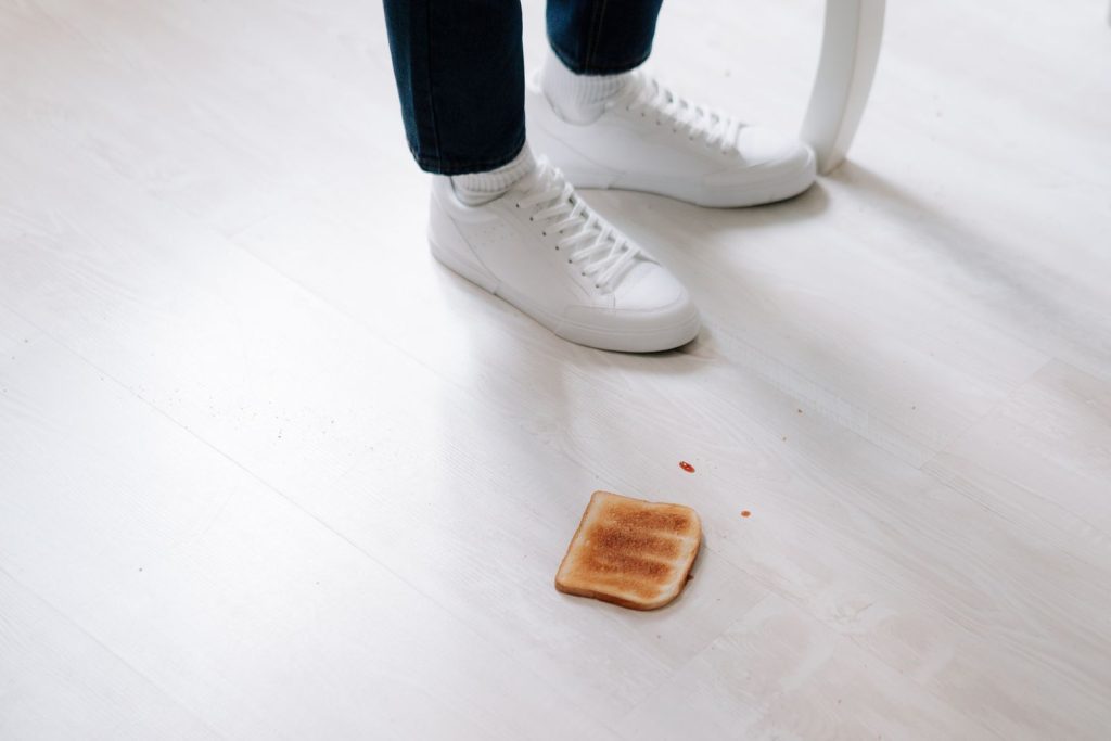 White sneakers next to a fallen piece of toast on a clean floor indoors.