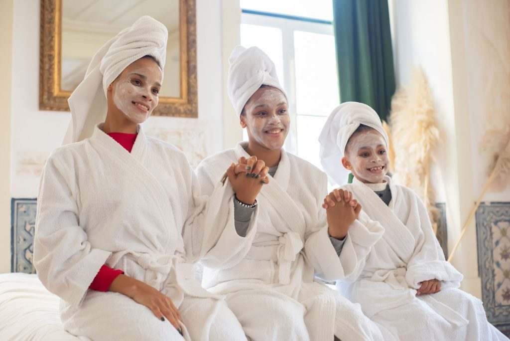 Mother and daughters enjoying a home spa day with face masks and bathrobes, exuding joy and relaxation.