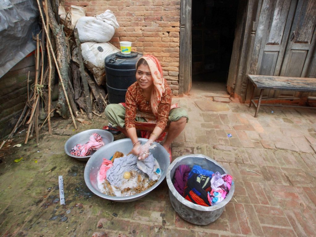 A woman hand washing clothes outdoors with multiple bowls around her in a rural setting.