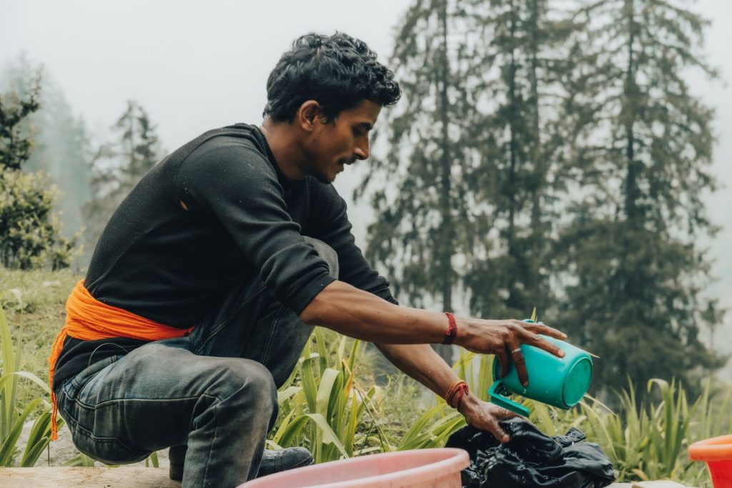 A man enjoys doing laundry outdoors surrounded by lush greenery and tall trees, capturing a moment of leisure and connection with nature.