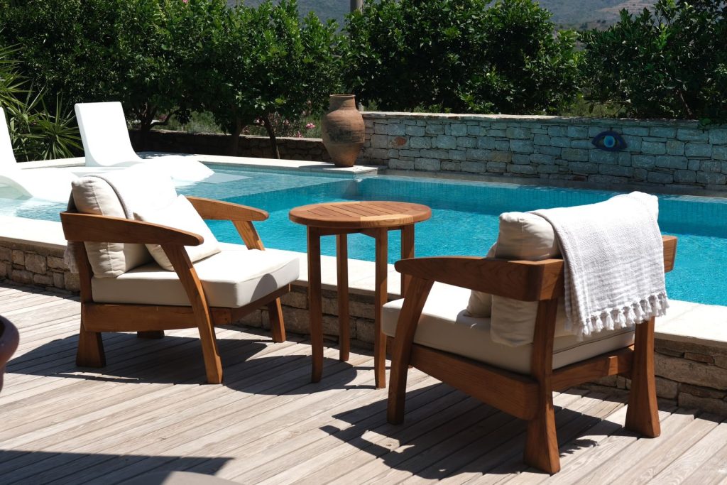 A serene poolside setup featuring two cushioned wooden chairs and a table, perfect for relaxation.