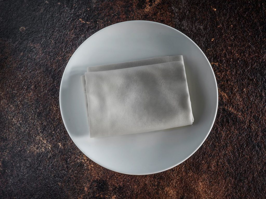 Simple white plate with a neatly folded napkin on a textured surface, perfect for dining themes.